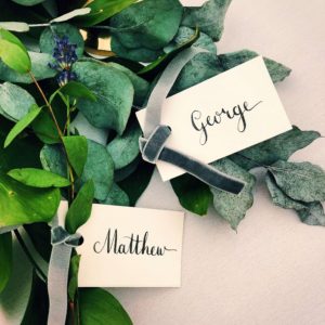 Wedding calligraphy place names black ink on white card on foliage